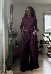 Bourgognefarvet langærmet top og viddebukser lavet af glat stof, med tilpasset talje og flydende design; ledsaget af solbriller og tilbehør.