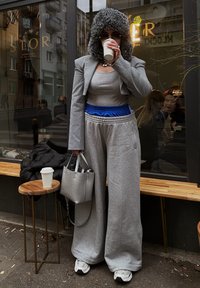 Hallide hallid hallid sinise vöökohtadega, hall crop bleiser ja hall tank top. Karusnahaga kaetud kapuuts, hõbedane käekott ja valge tass käes.