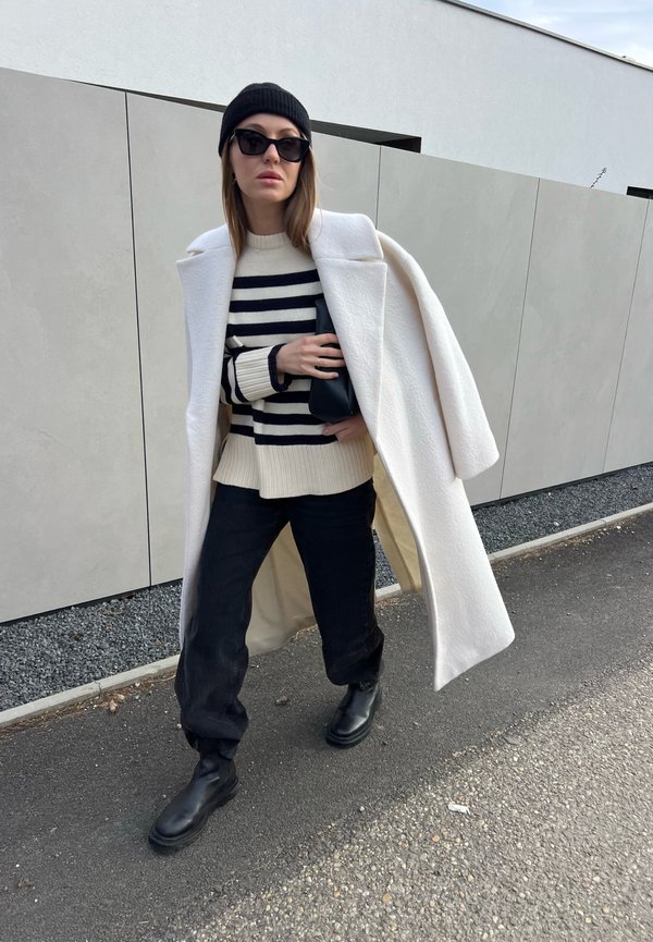 Vitt overskott, randig krämfärgad och marinblå tröja, svarta byxor, svarta stövlar och en svart clutch. Tillbehör inkluderar en svart mössa och solglasögon.