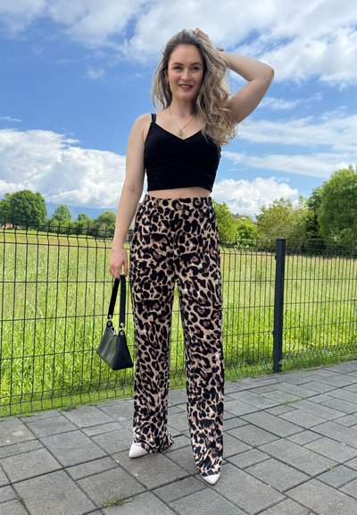 Pantalones de pierna ancha con estampado de leopardo en beige y negro, combinados con un top corto negro. Los accesorios incluyen un pequeño bolso negro y tacones de punta.