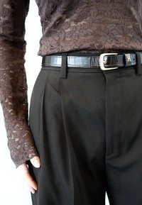 Vrchný diel z tmavohnedého čipkovaného materiálu s dlhými rukávmi, skombinovaný s čiernymi plisovanými nohavicami a lesklým čiernym opaskom so striebornou prackou a reliéfnymi detailmi.