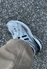 White and black athletic shoe with mesh and synthetic materials, featuring a textured upper, black accents, and a cushioned sole.