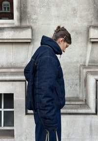 Polsterēta tumši zila džinsa jaka ar augstu apkakli, kontrastējošu šuvju izšuvumu un sānu kabatām. Valkāta kopā ar atbilstošām biksēm.