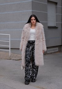 Hosszú világos rózsaszín műszőrme kabát, fehér, testhez simuló felső, fekete virágmintás, bő szárú nadrág és vastag fekete platform cipők.