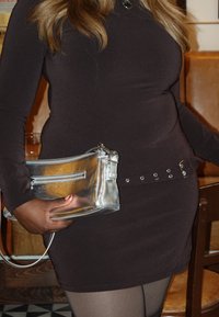 Strieborná metalická kabelka na zips s dvoma priehradkami, hladkou textúrou a odnímateľným remienkom, držená na tmavých šatách.