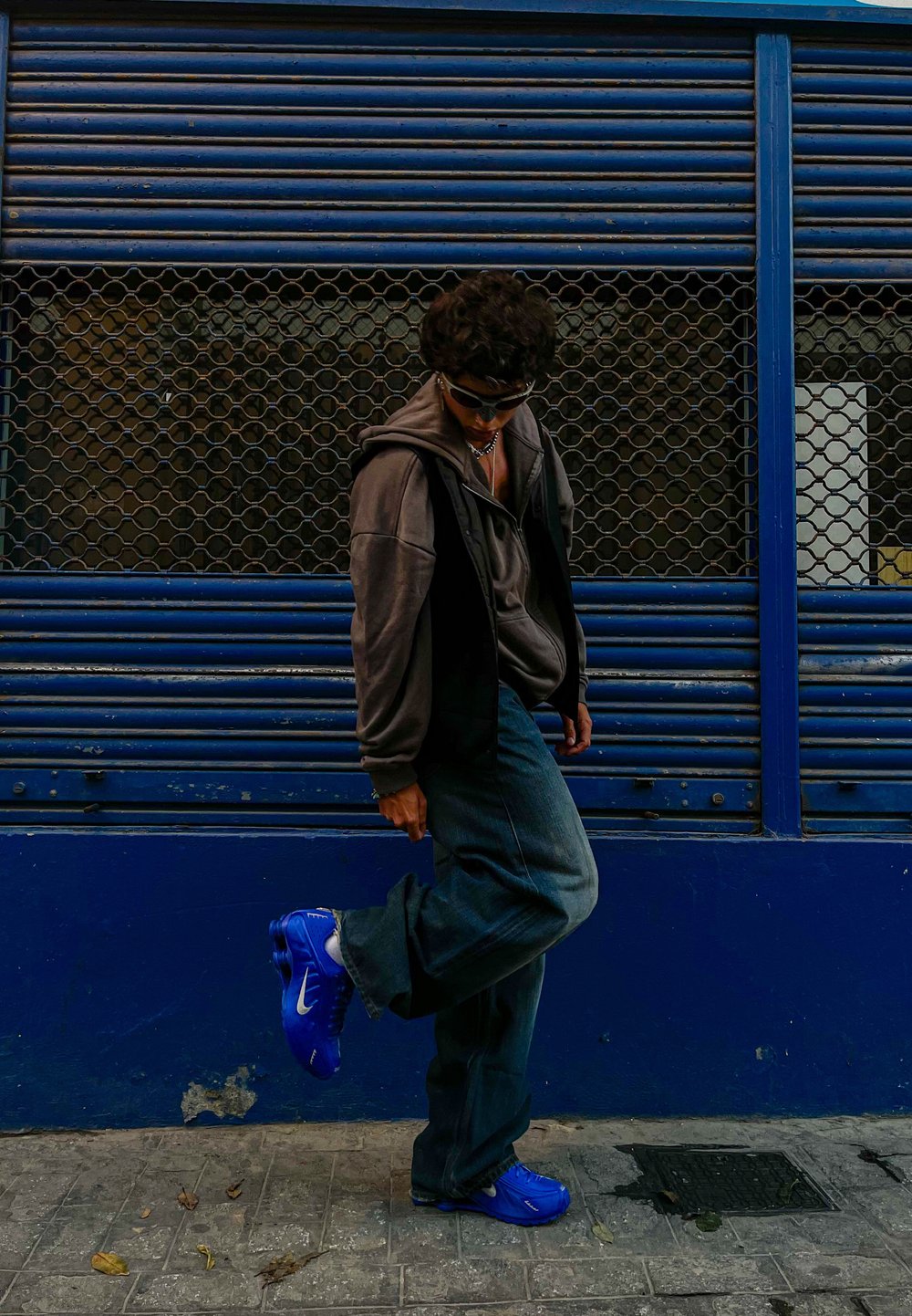 Μπλε αθλητικά Nike με υφή στο πάνω μέρος, συνδυασμένα με φαρδιά γκρι τζιν και σκούρο φούτερ, σε φόντο από μπλε και μαύρο διχτυωτό σχέδιο.