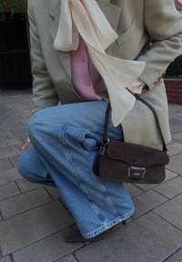 Brun mockaskinnsaxelväska med en rundad klaff och silverfästen, parat med ljusblå vida jeans och en rutigt blazer.