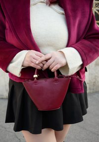 Geantă mică bordo, cu design structurat, textură netedă de piele și mâner rotund. Purtați cu o fustă închisă la culoare și o jachetă bordo.