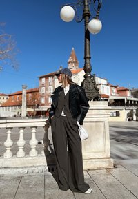 Casaco de couro preto, colete cinzento e calças largas cinzentas. Os acessórios incluem uma chapéu de denim e uma mala branca. O fundo apresenta um candeeiro de rua e edifícios.