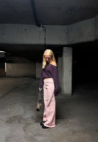 Överdimensionerad mörklila tröja med axeldetaljer, kombinerad med ljusrosa vida byxor. Svarta klumpiga skor och en leopardmönstrad handväska.