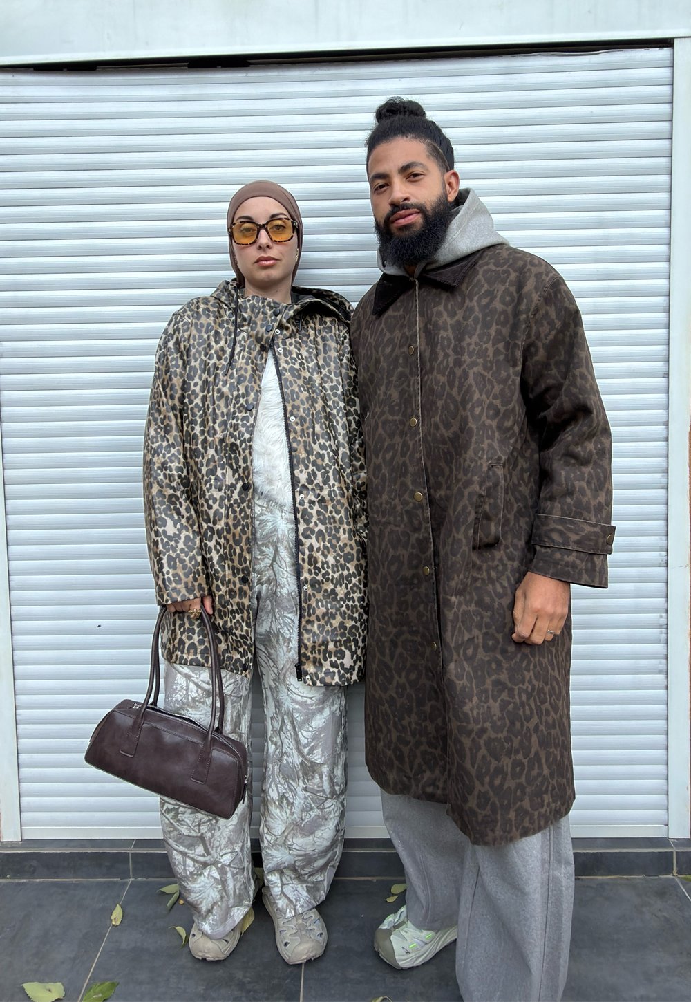 Manteau et pantalon imprimé léopard aux nuances de brun et beige, assortis à une tenue grise texturée et un sac à main marron, sur un fond clair.