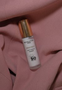 Revolution Pro Protect Soft Focus Primer i en hvit tube med gullkork, med SPF 50 og pro-alder etikett, hviler på myk rosa stoff.