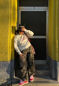 Sweat-shirt blanc avec texte "Paris Le Marais", pantalon large à motif camouflage, sneakers rouges avec accents roses, et un chapeau noir et crème à oreilles de chat.