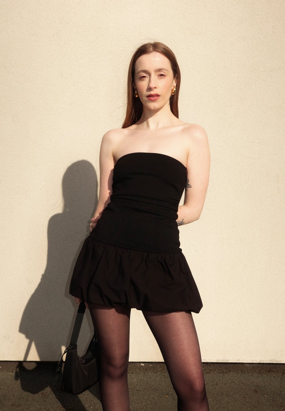Haut noir sans bretelles associé à une mini-jupe noire évasée, des collants noirs transparents et un petit sac à bandoulière. Tissu lisse avec un look élégant.