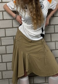 Weisses Sporttrikot mit Logo und orangefarbigen Akzenten, kombiniert mit einem khakifarbigen A-Linien-Rock mit Taschen, Bindebändern und einem ausgestellten Saum.