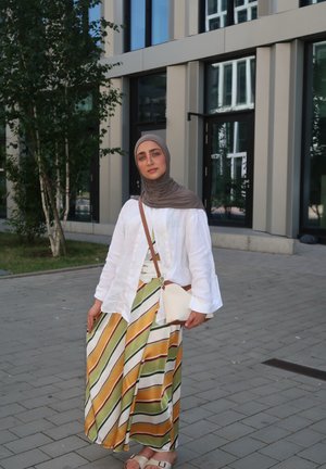 Camisa de lino blanca, falda maxi a rayas de colores en verde, amarillo y blanco, y un pequeño bolso blanco con una correa marrón.