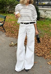 Rutet hvit og marineblå genser, løs passform, kombinert med høy midje hvite vide jeans. Svart belte og håndveske, holder en kaffekopp.