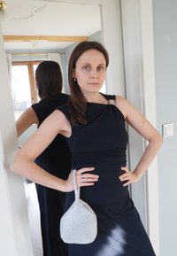 Robe noire sans manches avec un design drapé et des accessoires en argent. Tenant un petit sac à main argenté étincelant avec une forme unique et une bandoulière.