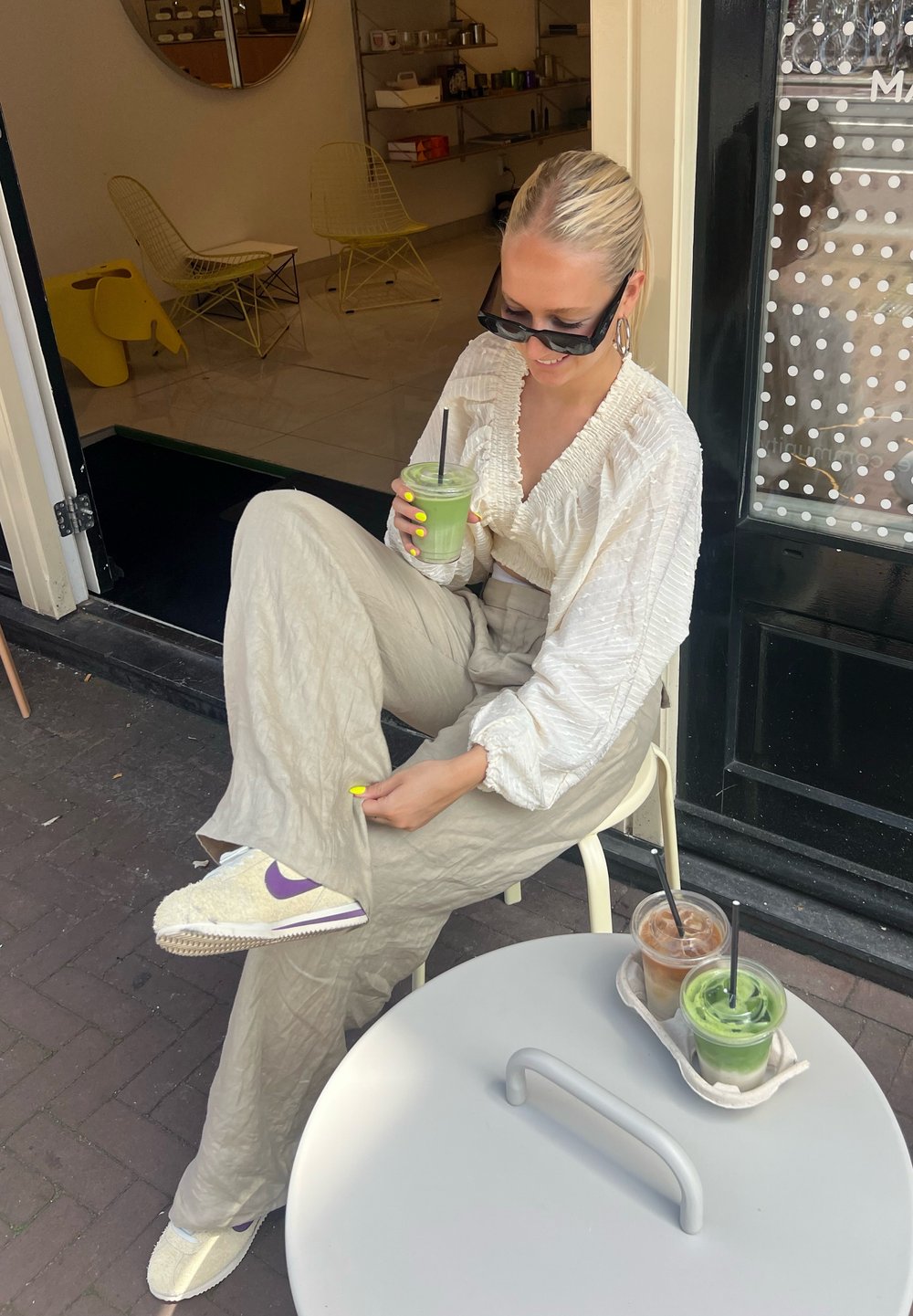 White textured cropped top, beige wide-leg trousers, and cream and purple trainers. Green and brown drinks on a light grey table.
