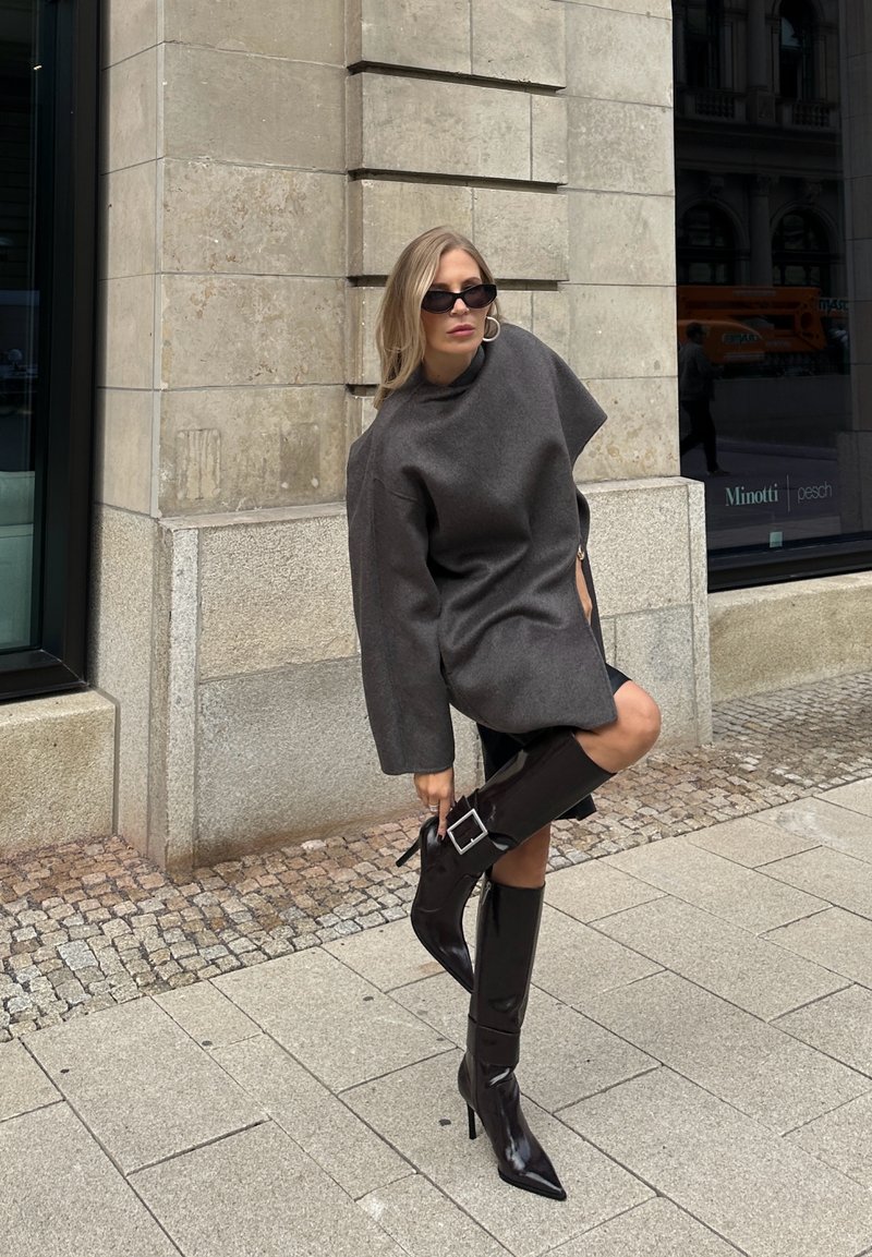 Gray oversized wool sweater with a high neck, paired with knee-high black patent leather stiletto boots featuring a buckled accent.