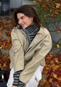 Beige oversized jacka över en grå och svart randig tröja, sittande på färgglada höstlöv, med en texturerad vit filt.