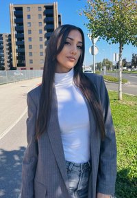 Γκρι σακάκι με ρίγες φορεμένο πάνω από λευκό ζιβάγκο, συνδυασμένο με τζιν σορτς ψηλής μέσης. Μακριά ίσια μαλλιά; υπαίθριο αστικό περιβάλλον.