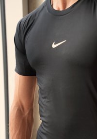 Svart tilpasset treningsskjorte laget av fukttransporterende stoff, med korte ermer og en liten hvit Nike-logo på brystet. Glatt tekstur.