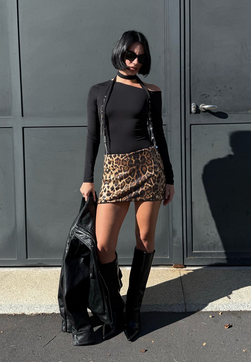 Sort langærmet bluse, miniskirt i leopardprint, sorte knæhøje støvler og læderjakke. Accessories inkluderer solbriller og en choker.