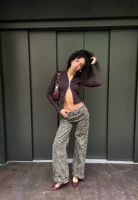 Háčkovaný, so zipsom, tmavofialový krátky sveter; široké nohavice s leopardím vzorom; bordové vysoké podpätky; kabelka cez rameno; textúrované kučeravé vlasy.