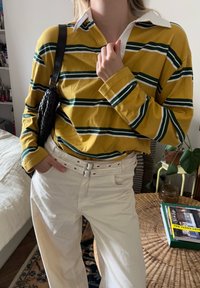 Langärmliges gelbes Hemd mit grünen und weißen Streifen, weißem Kragen; kombiniert mit hochtaillierten weißen Hosen und einer schwarzen geflochtenen Tasche.