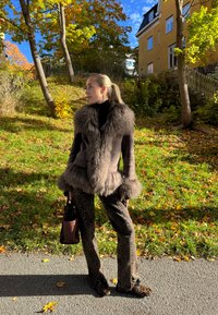 Palton din blană artificială cu guler și tiv gros, asortat cu pantaloni maro cu model și pantofi cu imprimeu leopard. Geanta maro completează ținuta.