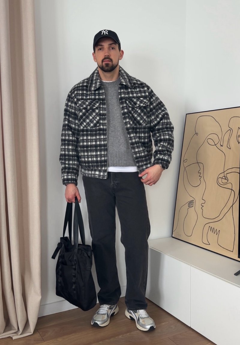 Veste à carreaux noir et blanc, pull gris, jeans noirs, baskets argentées et sac fourre-tout noir. Art linéaire minimaliste en arrière-plan.