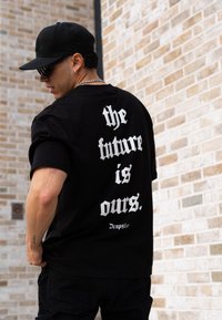 Black t-shirt with white text on the back reading "the future is ours." and "Dropsiz", featuring a relaxed fit and short sleeves.