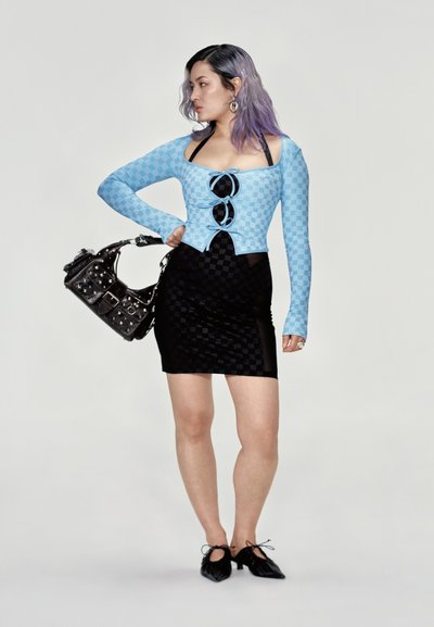 Top de manga larga azul claro con un patrón de cuadros y recortes, combinado con una falda negra ajustada. Los accesorios incluyen un bolso negro con tachuelas.