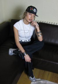 Mustapanta, jossa on kukkakirjontaa ja New York -logo, valkoinen istuva t-paita, hopeaketju, hopea-rannekoruja, väljät siniset farkut ja metalliset lenkkarit.