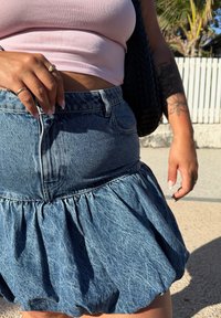 Denim nederdel med sammensamlet kant, lys blå vask, høj talje, frontlommer og en struktureret overflade. Accepteret af en pink crop top.