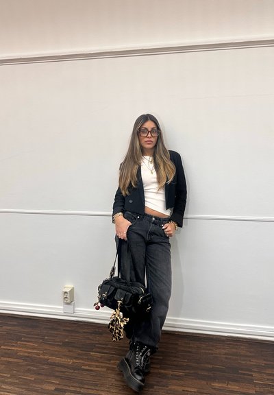 Blazer negro recortado sobre una blusa blanca, combinado con jeans negros de cintura alta. Los accesorios incluyen un bolso negro y botas de combate.