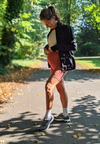 Sportinė apranga, sudaranti iš šviesaus spalvos marškinėlių, tamsaus švarko ir mauve spalvos šortų; derinama su pilkais "New Balance" sportbačiais ir baltais kojinaitėmis.