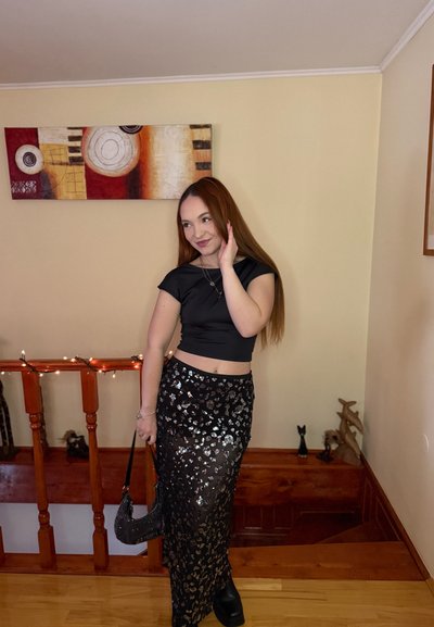 Top corto negro combinado con una falda negra con lentejuelas y un patrón floral. Los accesorios incluyen un bolso de cuentas y botas negras gruesas.