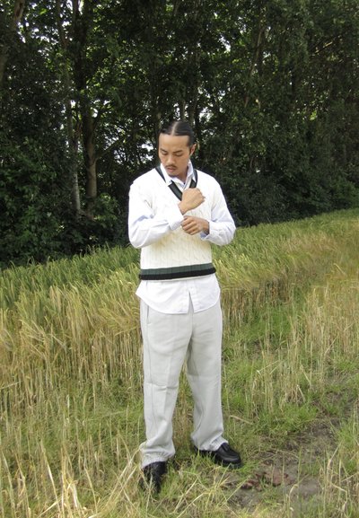Camisa blanca de manga larga con botones debajo de un chaleco de punto en color crema con detalles verdes, combinado con pantalones gris claro y zapatos negros.
