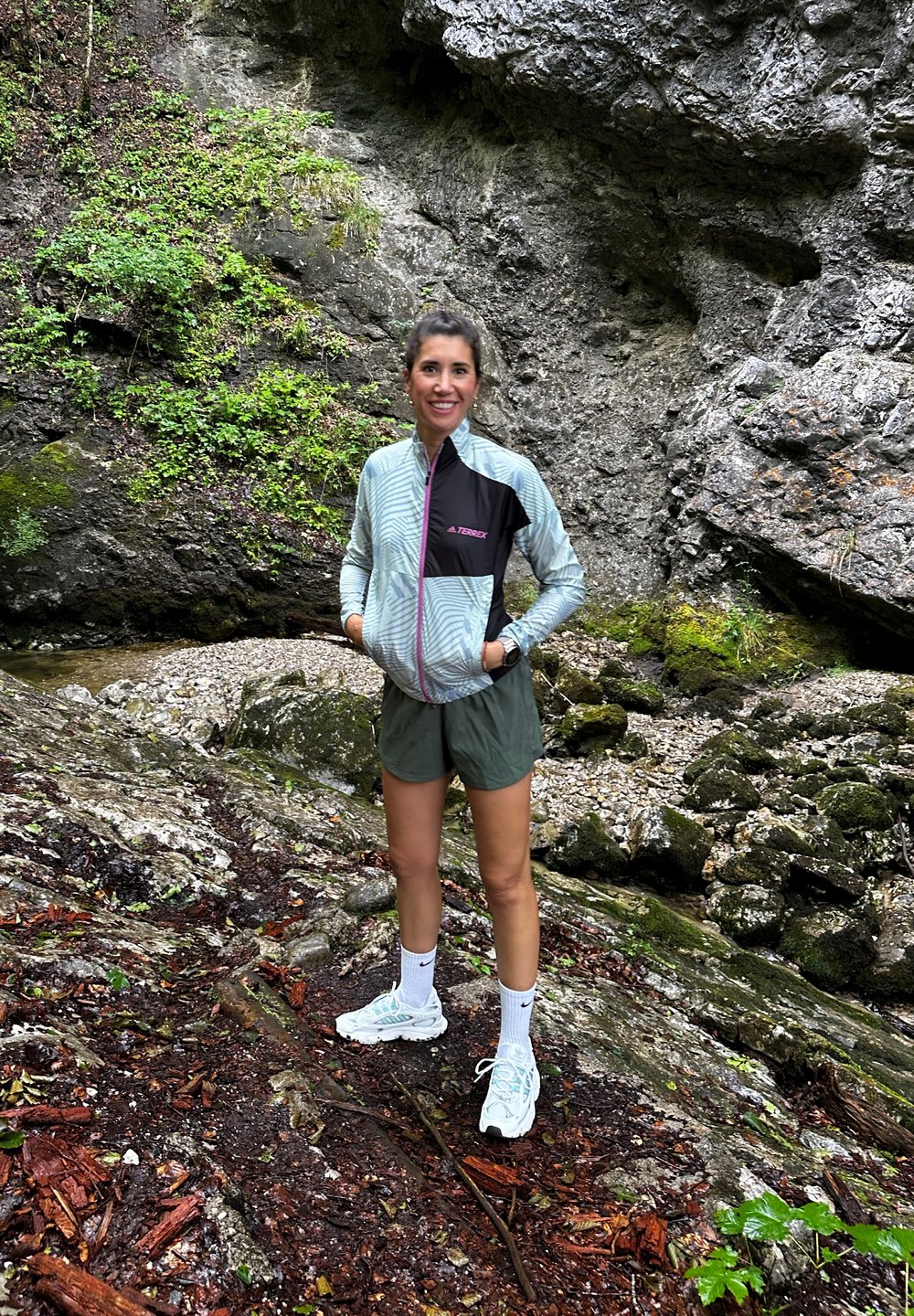 Svijetloplavi i crni zip-jakna s geometrijskim uzorkom, maslinasto zeleni šorts i svijetloplave sportske cipele na stjenovitom, prirodnom terenu.