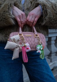 Ροζ υφασμάτινη τσάντα με χρυσές λεπτομέρειες, featuring μια μεγάλη μπεζ κορώνα και μπρελόκ με κινούμενα σχέδια ζώα. Οι λαβές είναι κοντές και ανθεκτικές.