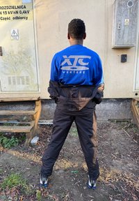 Blauw shirt met lange mouwen en het logo "XTC VERTERE", gecombineerd met een zwarte broek. Het materiaal lijkt lichtgewicht en heeft een casual pasvorm. Schoeisel met zilveren accenten.