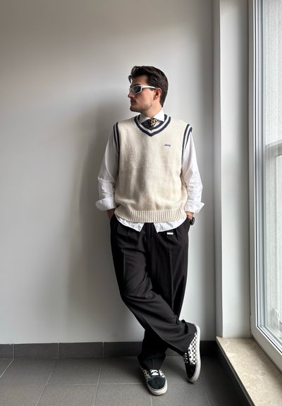 Saco de punto en crema sin mangas con ribete azul marino, sobre camisa blanca, pantalones negros con pliegues y zapatillas a cuadros. Las gafas de sol completan el look.