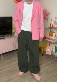 Ljusrosa blazer över en vit skjorta, kombinerat med mörkgröna vida byxor och rosa loafers. Accessoarer med ett silverkorshalsband.