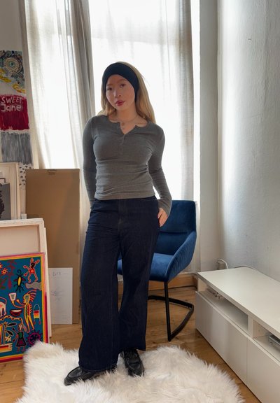 Camisa henley de manga larga gris combinada con jeans de pierna ancha azul oscuro. Una diadema negra acentúa el cabello claro. Textura sutil en las telas.