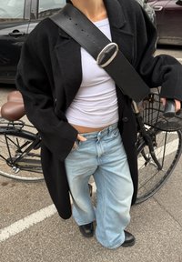 Czarny, oversize wełniany płaszcz, biały dopasowany koszula, jasnoniebieskie, szerokie dżinsy, czarny skórzany pasek z srebrną klamrą oraz czarne botki za kostkę.