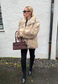 Valgekunstmõõdus beež karvkattega mantel, üle suurusega. Mustad retuusid, põlvikukõrgused teravate ninaosadega saapad tekstuuriga mustriga. Pruun käekott struktureeritud disainiga.