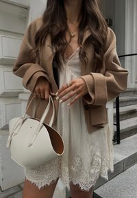 Brun uldblandet oversized jakke, hvid kjole med blonder, lysfarvet håndtaske med en struktureret silhuet og lædertekstur.