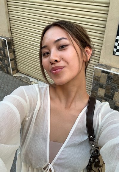 Top ligero y transparente de color blanco, con mangas largas, escote en V y detalle de cordón. Bolsa marrón con acentos de hardware visibles en la imagen.